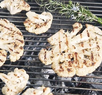 Bloemkoolsteaks en een takje rozemarijn grillen op een barbecue boven hete kolen.