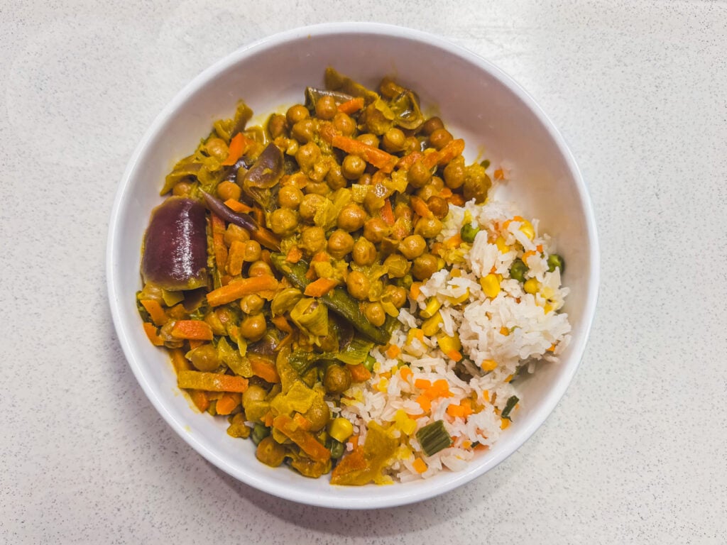 Een witte kom met aan de ene kant een curry van kikkererwten en groenten en aan de andere kant rijst met gemengde groenten, geplaatst op een lichtgekleurde ondergrond – slechts één voorbeeld van campusmaaltijden die zijn getest aan de VUB in Brussel.