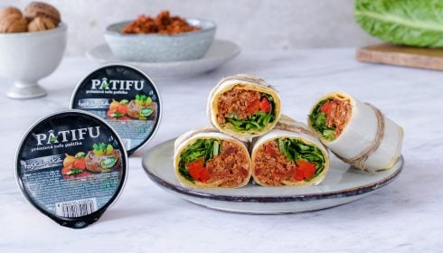 Čtyři zeleninová burritos plněná zeleninou, červenou paprikou a pomazánkou z tofu jsou vystavena na talíři vedle dvou nádob s paštikou z tofu Pátifu. V pozadí se na světlé ploše objevují vlašské ořechy, pomazánka s ořechovým květákem a salát.