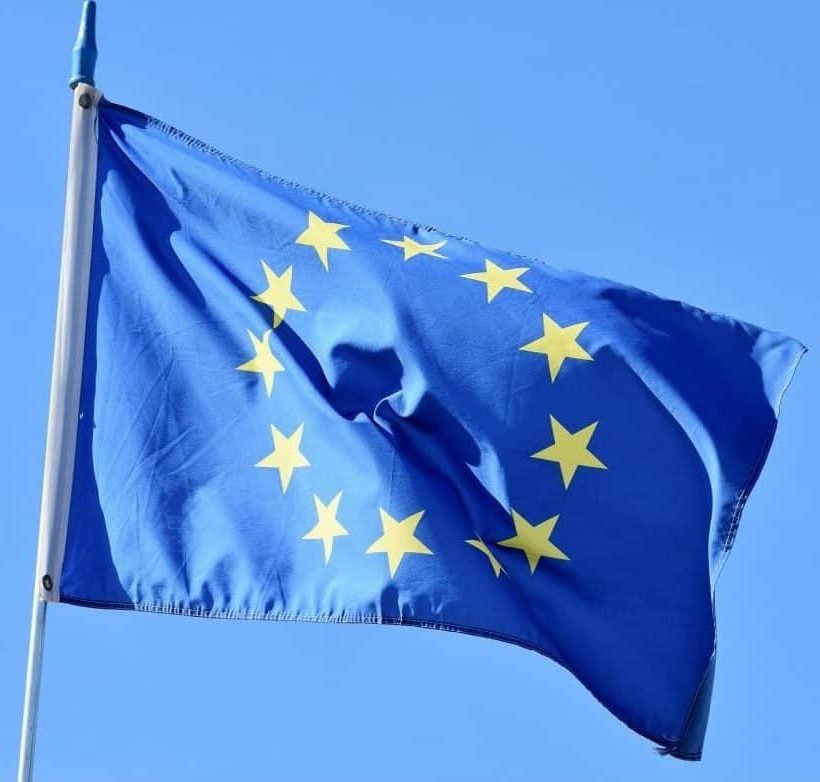 Eine blaue Flagge mit einem Kreis aus zwölf gelben Sternen, die die Europäische Union repräsentieren, weht vor einem strahlend blauen Himmel.