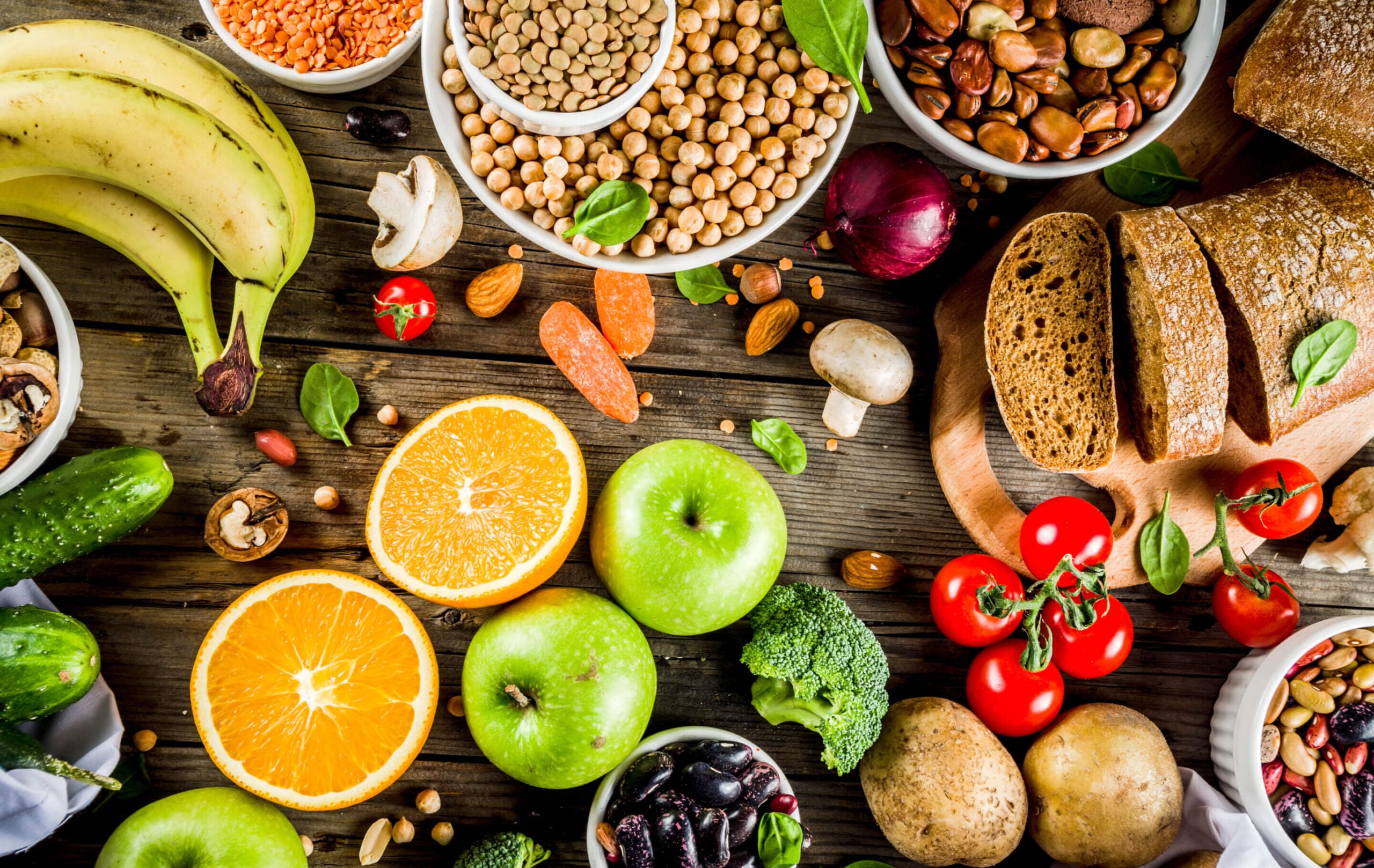 Una selección de frutas frescas, verduras, cereales integrales y legumbres dispuestas sobre una mesa de madera.