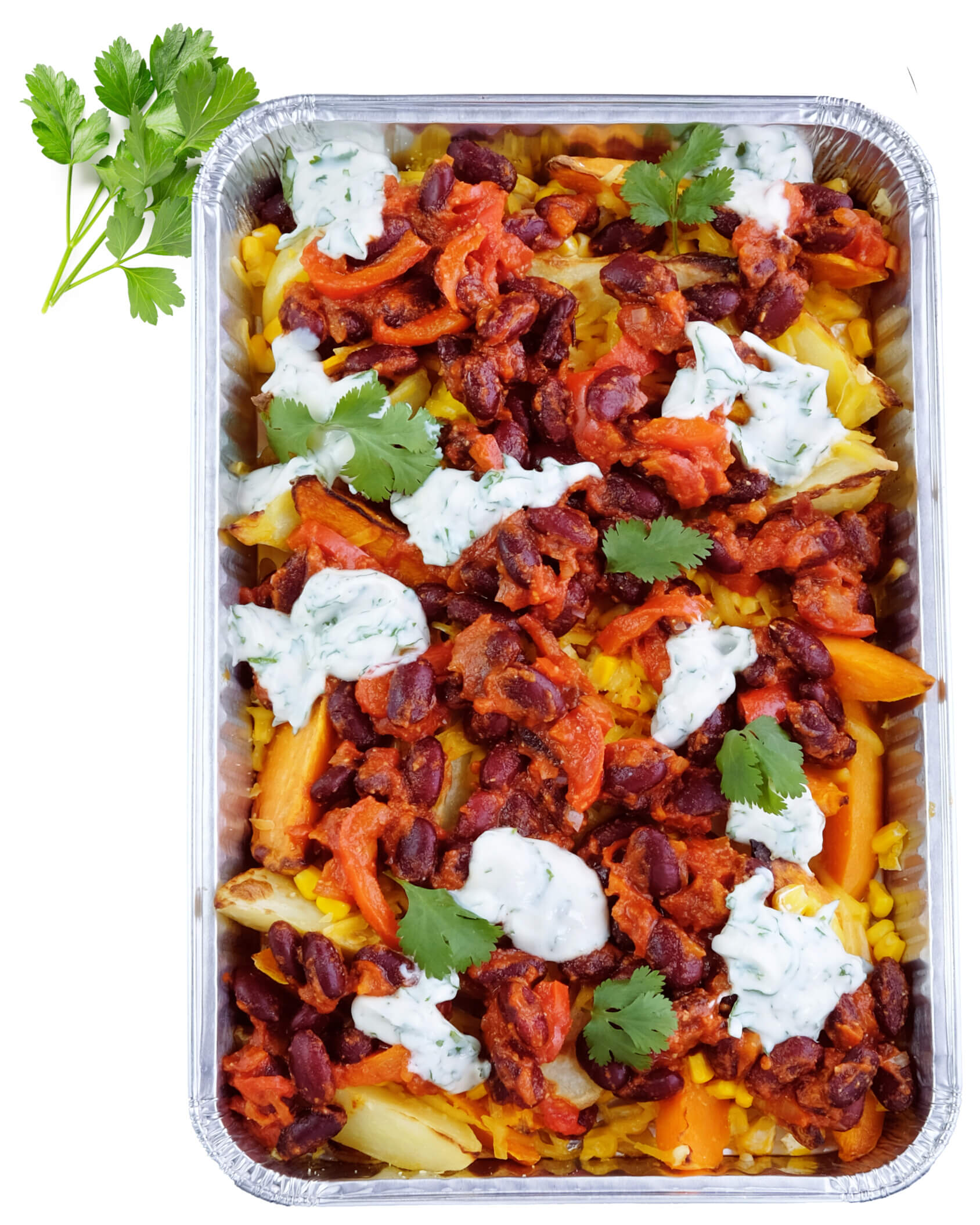 A foil tray filled with baked vegetables, kidney beans in tomato sauce, yellow rice, and topped with dollops of white herb sauce and fresh coriander. Parsley sprigs lie beside the tray.