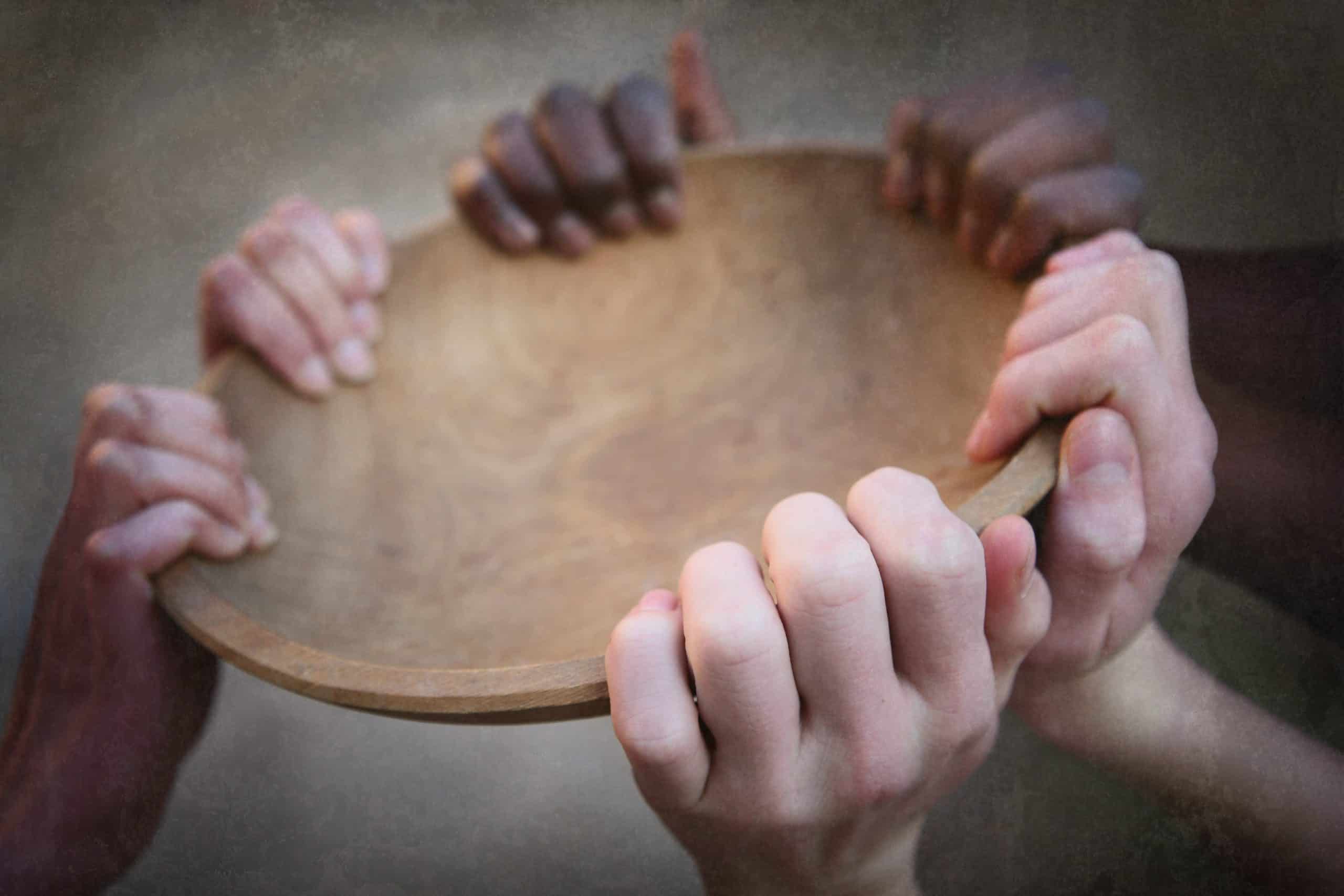 Hands of various skin colors holding onto an empty bowl