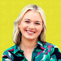A young woman with blonde hair smiles warmly at the camera. She is wearing a colorful, patterned shirt and is posed in front of a bright yellow background.
