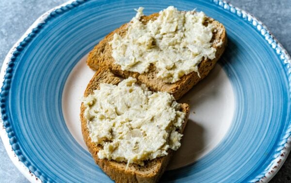 Two slices of brown bread topped with a creamy spread are placed on a blue and white plate, set on a grey surface.